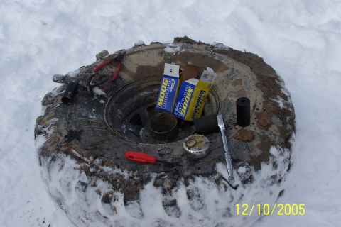 1979 Ford Bronco - A tire lies in the snow with various tools and MOOG brand parts scattered around it.