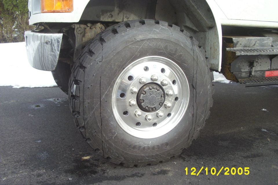 Polished aluminum 10-lug truck wheel with off-road tire on a white truck