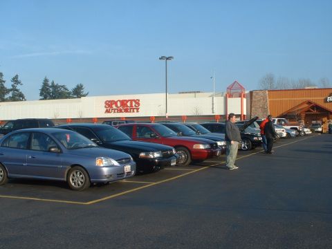 1999 Ford Crown Victoria - A group of cars are parked in a lot in front of a Sports Authority store on a sunny day.