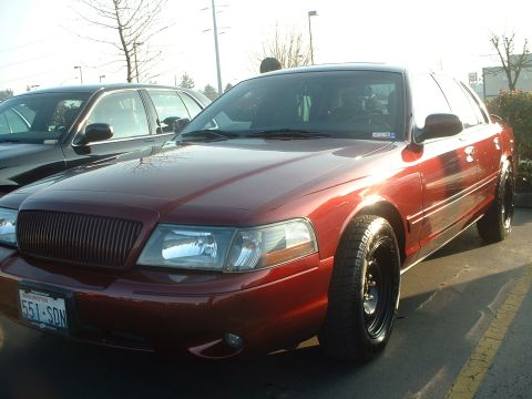 1999 Ford Crown Victoria - A red sedan, possibly a Mercury Grand Marquis, is parked in a lot.