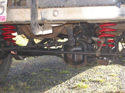 1991 Ford Explorer - Under-truck view of a solid front axle with red aftermarket lift coil springs on both sides, showing the cast differential housing, tie rod…