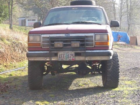 1991 Ford Explorer - Head-on view of a lifted red Ford Explorer on oversized mud-terrain tires, fitted with a tube grille guard, a spare tire on the roof and an…