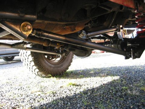 1991 Ford Explorer - Underside view of a lifted 4x4 front end on gravel, showing the black-painted solid front axle, radius arms, adjustable tie rod and drag li…