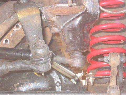 1991 Ford Explorer - Close-up of a 4x4 front suspension and steering with a red powder-coated coil spring, radius-arm mount, and two greasy tie rod ends threade…