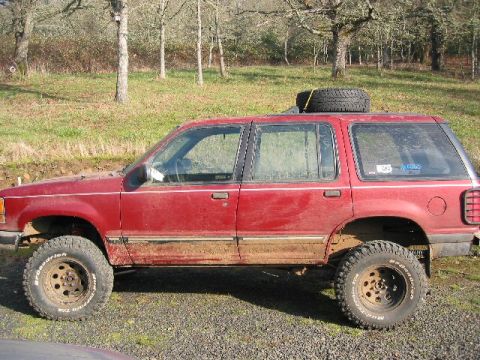 1991 Ford Explorer - A red 1991 Ford Explorer modified for off-road use sits parked outdoors.