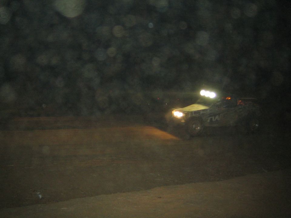 Distant off-road race truck with light bar driving on a dark desert course at night