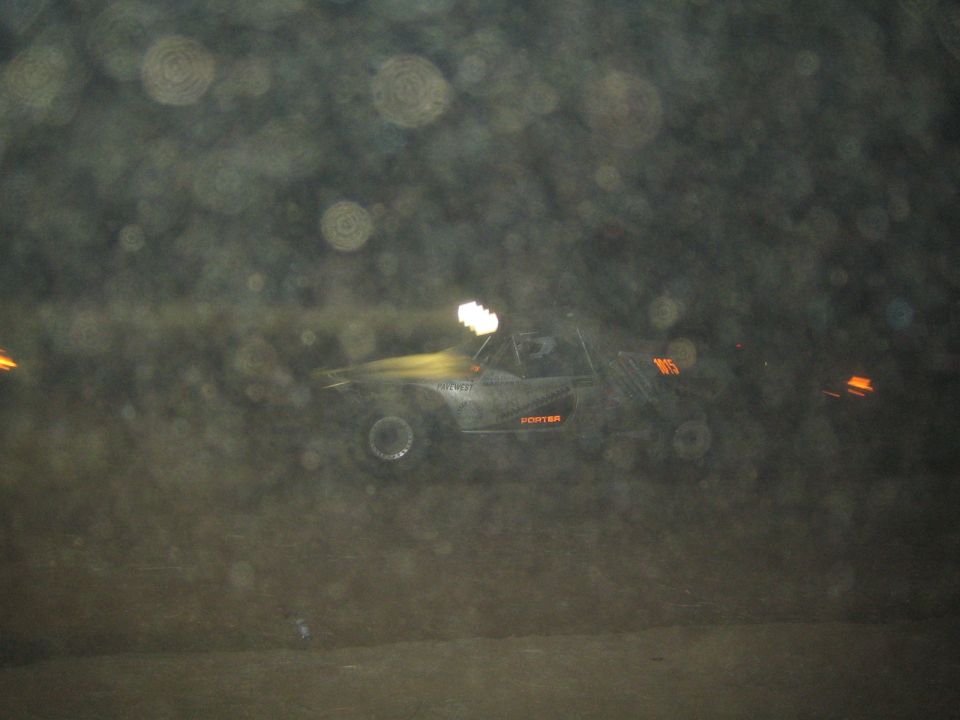 Dark off-road race car in motion blur with headlight glow on a night course