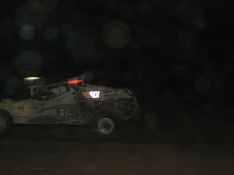 1990 Ford Bronco - decaled off-road race buggy marked 101 sits in profile on a very dark desert course at night with faint background lights.