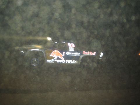 1990 Ford Bronco - dark off-road race truck bearing Red Bull, Toyo Tires and a charging bull logo streaks across a dusty night course.