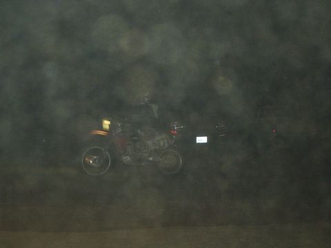 1990 Ford Bronco - dirt bike rider crosses a hazy dark desert course at night, the scene shrouded in a heavy misty speckled haze.