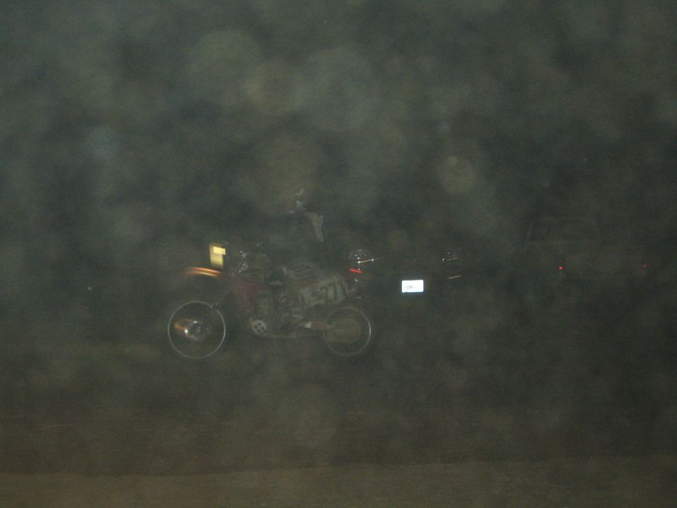 Dirt bike rider on a hazy dark desert course at night through a misty frame