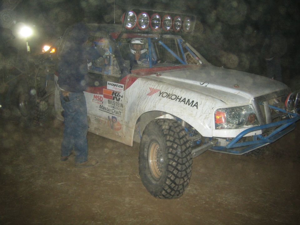 White off-road race truck with roof lights and Yokohama decal in lit pit at night