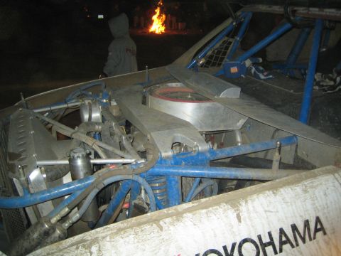 1990 Ford Bronco - exposed engine bay and blue tube chassis of an off-road race vehicle photographed at night beside a fire.