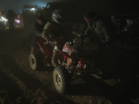 1990 Ford Bronco - rider sits on a red quad ATV at night while another person stands alongside in a dim off-road staging area.