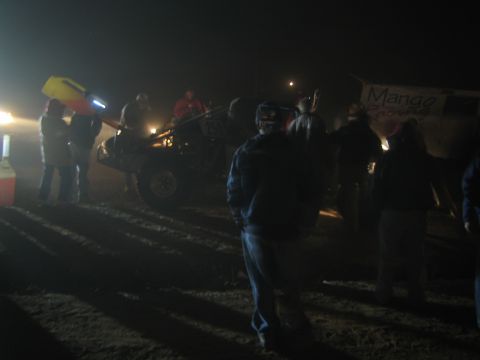 1990 Ford Bronco - People stand in a foggy nighttime desert pit, a race vehicle and a 'Mango Racing' banner lit in the background.