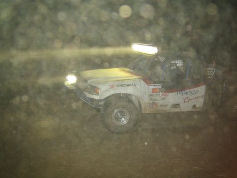 1990 Ford Bronco - yellow-and-white Mango Racing off-road truck races through the dark with its light bar blazing.