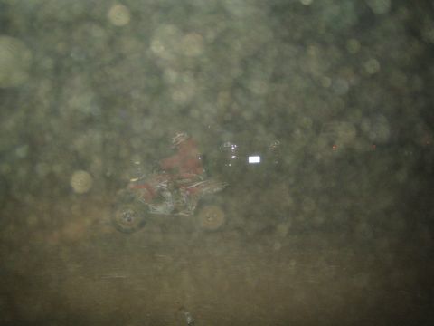 1990 Ford Bronco - red quad ATV moves through the darkness, dimly visible through a heavily spotted lens.
