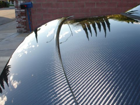 1993 Ford Taurus - Close-up of a car's carbon fiber hood, reflecting the surrounding environment.
