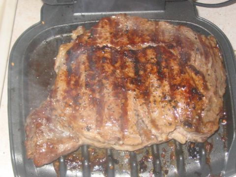 1991 Ford Bronco - A thick cut of meat is being grilled, showing distinct grill marks and some smoke rising.