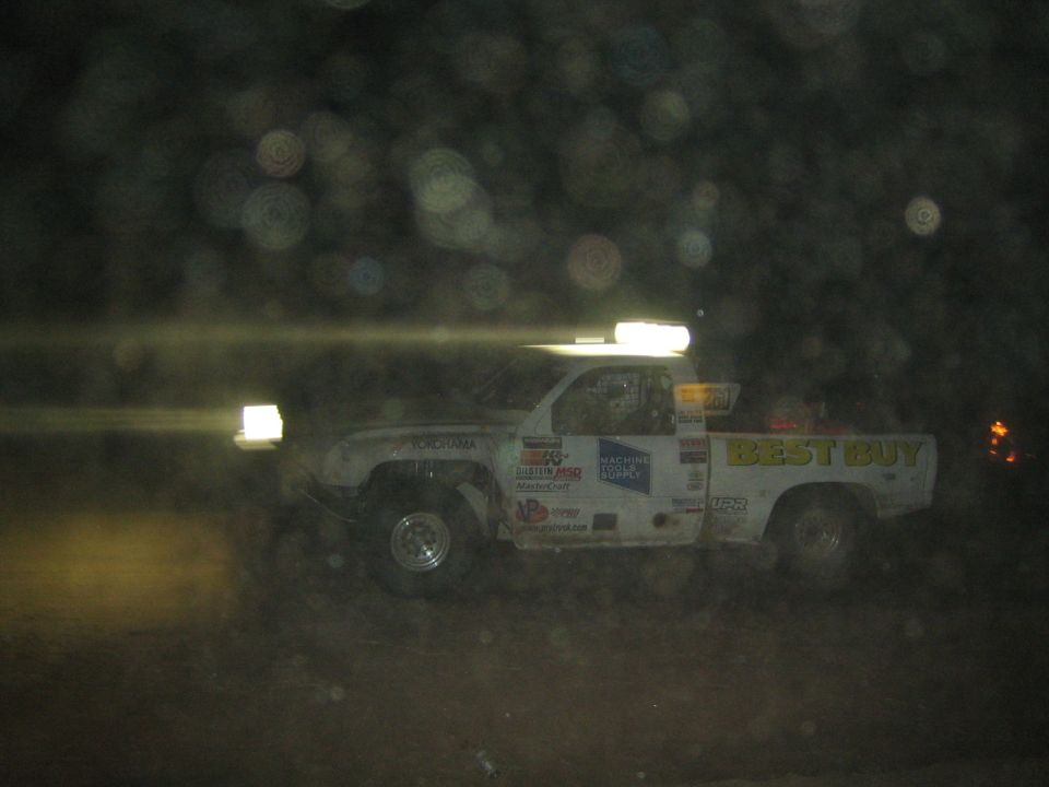White off-road race truck with 'Best Buy' livery racing at night, lights on