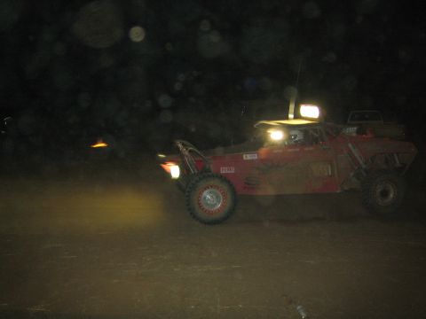 1990 Ford Bronco - red off-road race buggy runs at night with its overhead light bar glowing, seen through a spotted lens.