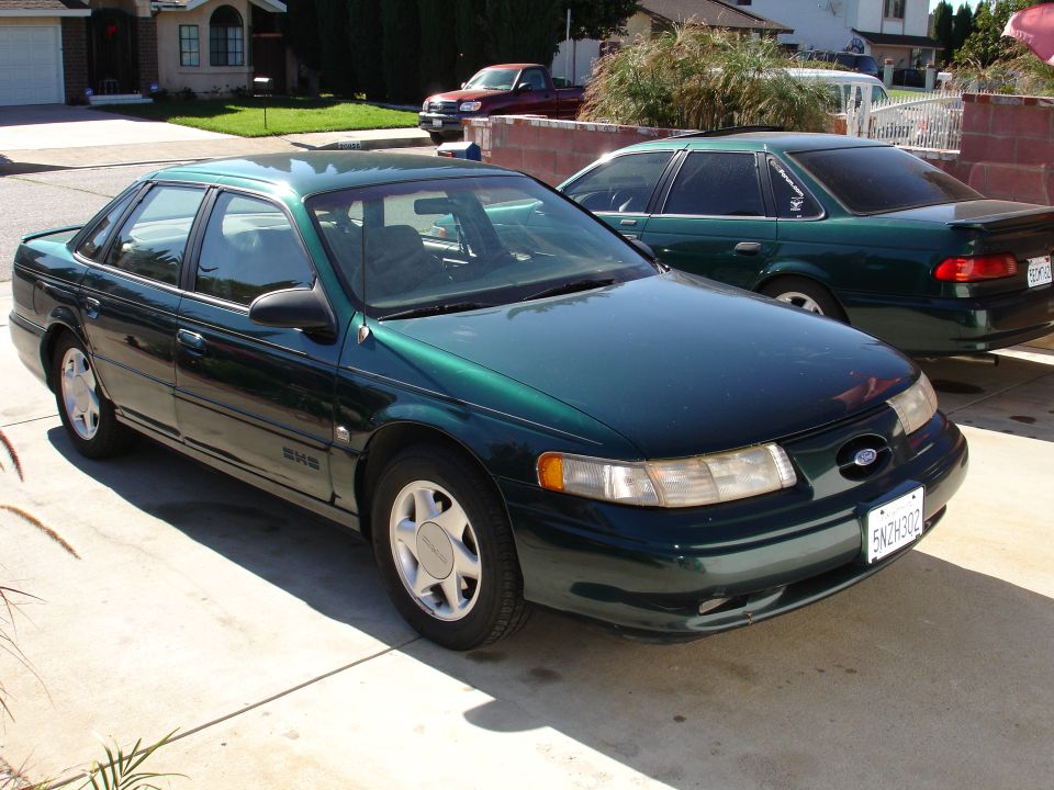 Green sedan parked in a driveway, front 3/4 view. Visible badge on grille, license plate 5NZH302