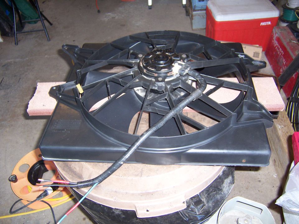 Black electric radiator cooling fan and shroud assembly lying on a garage floor