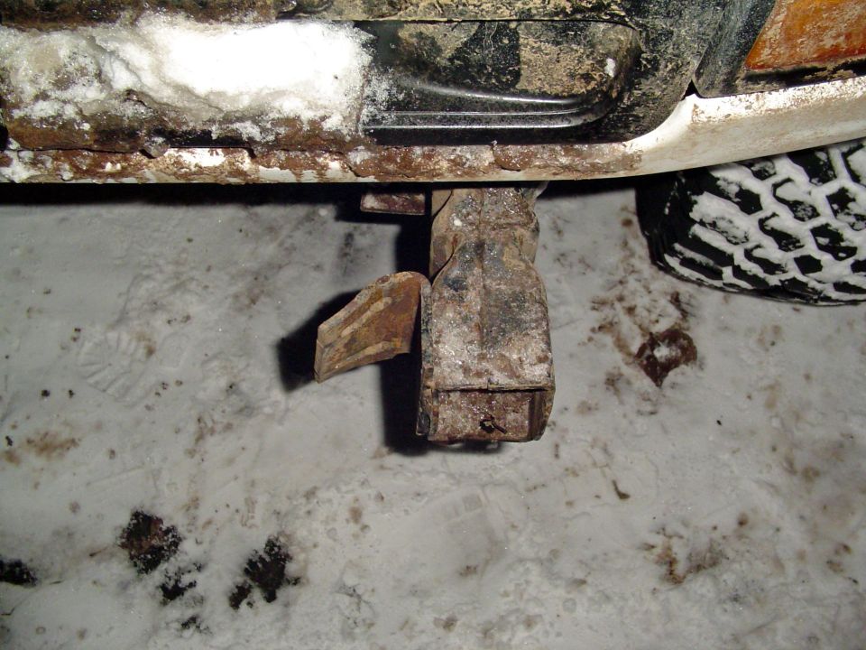 Rusted metal bracket attached to undercarriage of vehicle, with tire visible in snow