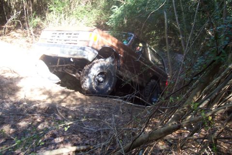 1987 Ford Bronco - This off-road vehicle appears to be stuck in a muddy, wooded area, with its tires deep in the mire.