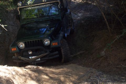 1987 Ford Bronco - A green Jeep Wrangler navigates a challenging off-road trail, its front tires deep in mud.