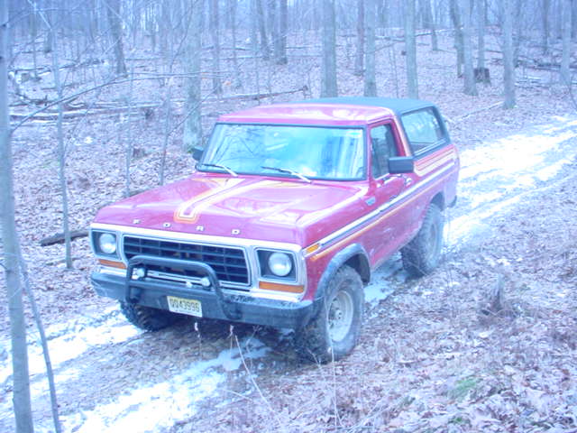 Red 1979 Ford Bronco with black brush guard on a snowy trail through leafless woods