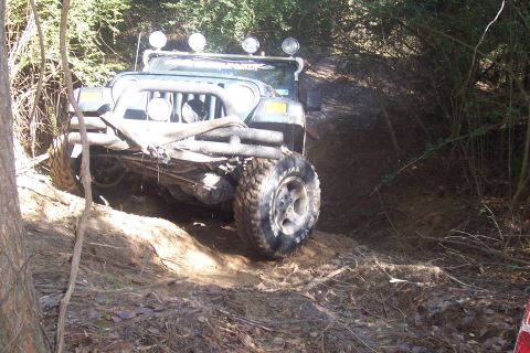 1987 Ford Bronco - A green Jeep Wrangler TJ tackles a challenging off-road course, demonstrating its capabilities on a steep, muddy incline.