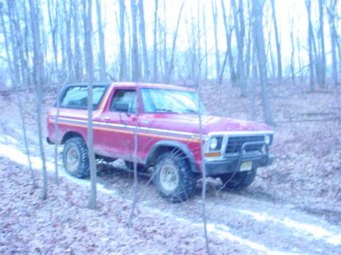 1979 Ford Bronco - A red Ford Bronco navigates a wooded area with snow on the ground.