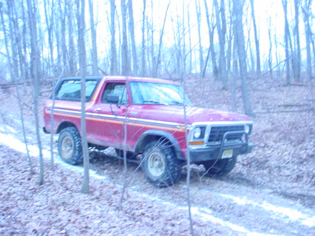 Red Ford Bronco driving on a snowy dirt road through trees