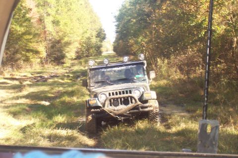 1987 Ford Bronco - A Jeep Wrangler navigates a challenging off-road path through a wooded area.