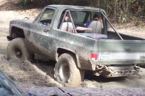 1987 Ford Bronco - This pickup truck is stuck in mud, showing its rear end and a roll cage.