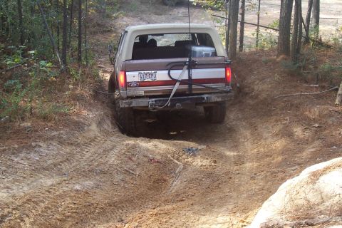 1987 Ford Bronco - A 1987 Ford Bronco navigates a challenging dirt trail in a wooded area.