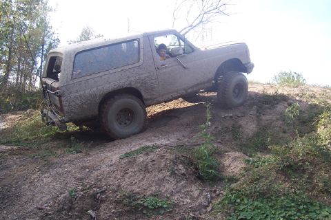 1987 Ford Bronco - This SUV is covered in mud as it navigates a challenging off-road terrain.