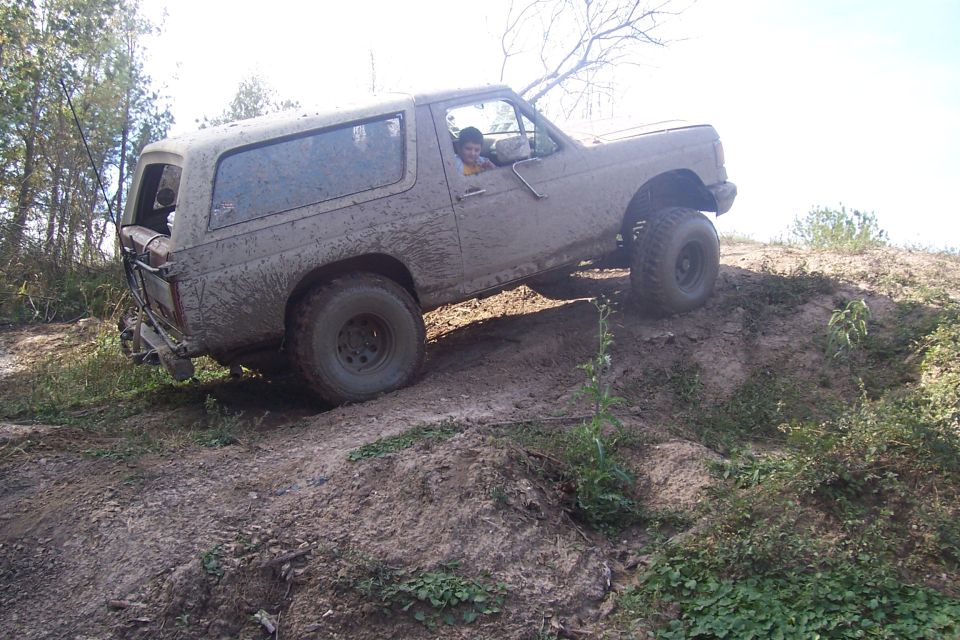 Muddy SUV climbing a dirt hill. Driver visible inside