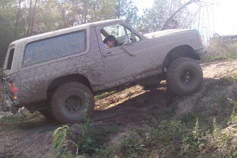 1987 Ford Bronco - This SUV is covered in mud as it navigates an off-road trail.
