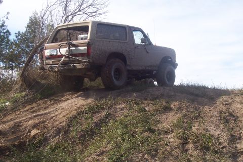 1987 Ford Bronco - This 1987 Ford Bronco is shown climbing a muddy dirt hill, highlighting its off-road capabilities.