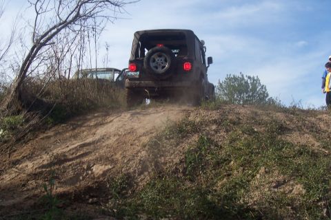 1987 Ford Bronco - A Jeep Wrangler ascends a sandy incline, kicking up dust. Another vehicle is visible in the background.
