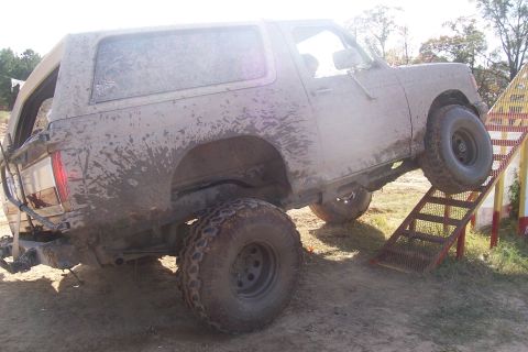 1987 Ford Bronco - This off-road vehicle is covered in mud as it ascends a ramp, suggesting it has been used for recreational driving.