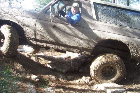 1987 Ford Bronco - A driver navigates a heavily mud-caked SUV over a rocky, off-road trail.