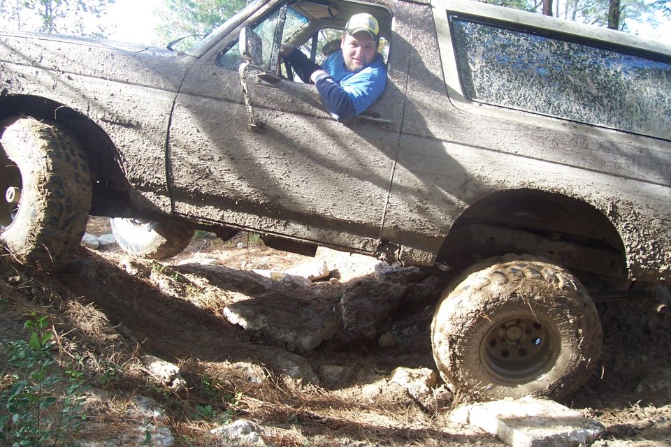 Muddy SUV climbing over rocks with driver visible