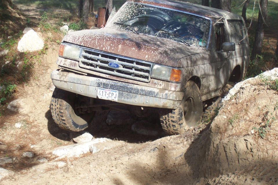 Mud-covered 1987 Ford Bronco navigating an off-road trail