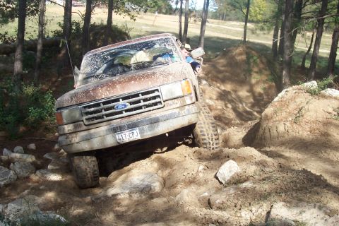 1987 Ford Bronco - 1987 Ford Bronco tackling a challenging off-road trail with mud and rocks.