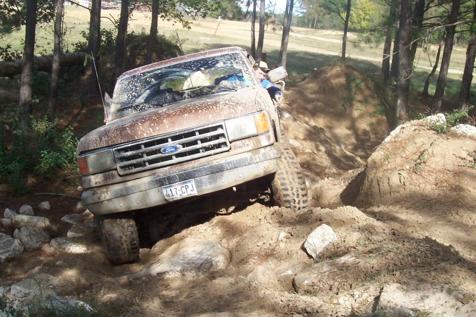 Brown 1987 Ford Bronco navigating a rocky, muddy off-road course
