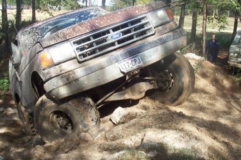 1987 Ford Bronco - A brown Ford truck navigates a challenging off-road course, with another vehicle and a person visible in the background.