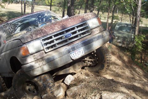 1987 Ford Bronco - A muddy 1987 Ford Bronco navigates an off-road trail, with another vehicle visible in the background.